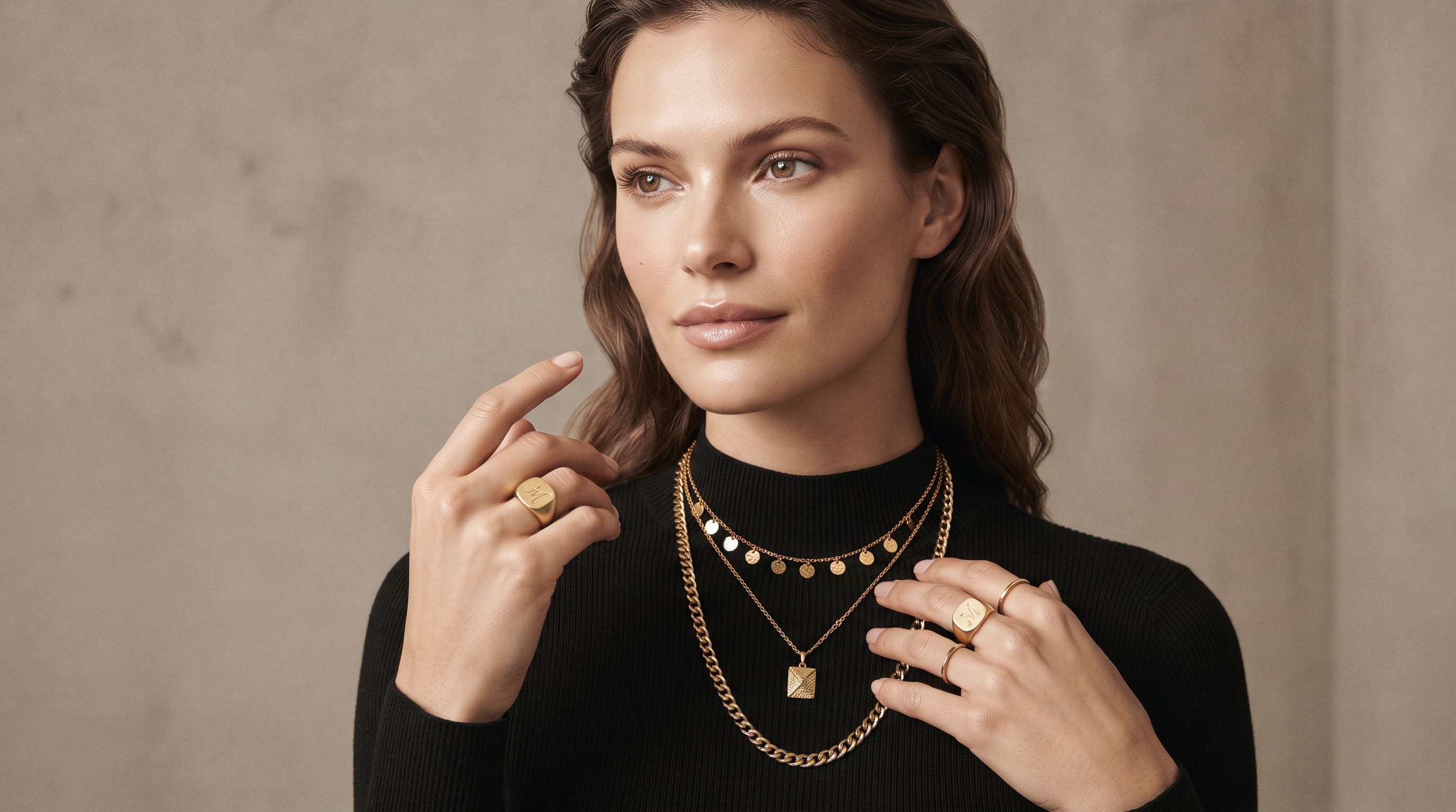 Model wearing layered gold necklaces and a signet ring
